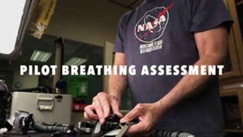 A person in a NASA t-shirt holding and adjusting breathing equipment.
