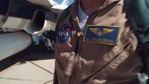Close-up of a pilot's flight suit showing NASA patches and an American flag.