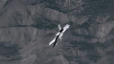 An aircraft flying through the sky and banking sharply over a mountain range.