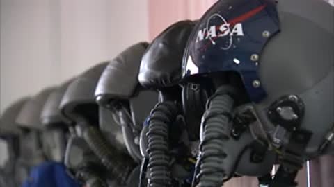 A row of pilot helmets with attached oxygen masks lined up on shelves.
