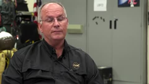 Man in black shirt speaking in an indoor setting.