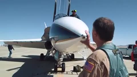 Pilot standing by the nose of a parked jet on the tarmac.