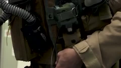 Connecting a breathing hose to flight gear while man talks in insert.