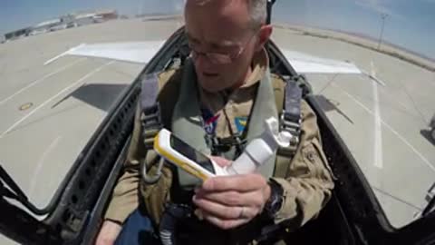 Pilot sitting in cockpit holding a device and checking equipment.