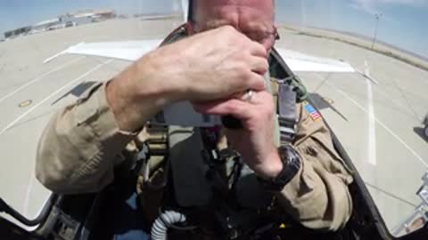 Pilot adjusting helmet and gear inside an aircraft cockpit.
