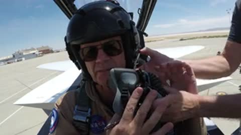 Pilot in cockpit being assisted with attaching an oxygen mask.