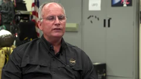 Man speaking in black shirt in front of an equipment background.