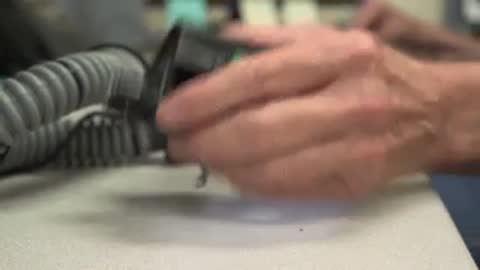 Hands inspecting small black electronic device on desk.