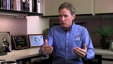 Man in blue shirt talking in office environment.
