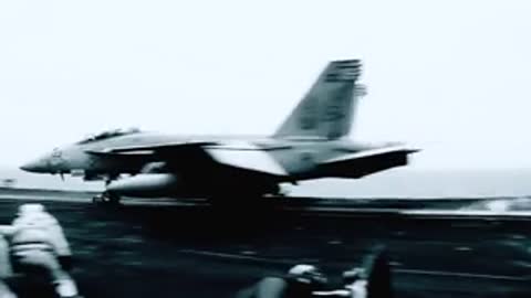 Military jets parked on an aircraft carrier flight deck near mountains.