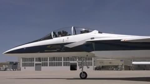 Fighter jet parked on tarmac outside hangar.