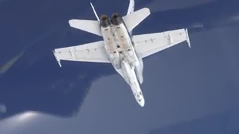 Top view of a fighter jet in flight, then a pilot speaking inside a hangar.