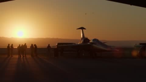 Silhouette of X-59 aircraft parked outside hangar at sunrise.