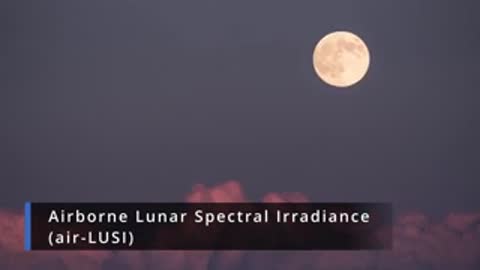 View of the full moon in the dark sky above pinkish clouds.