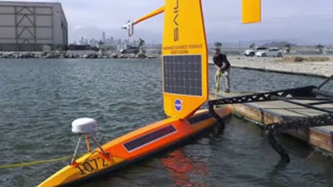 Ocean waves swirling around a yellow autonomous surface vehicle docked near a coast.