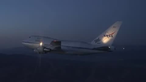A NASA SOFIA Boeing 747 aircraft flying in the night sky with lights on.