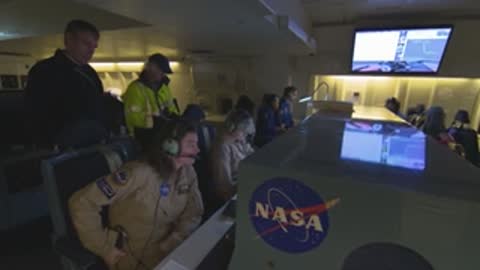 People working inside a NASA flight deck with monitors displaying flight data.