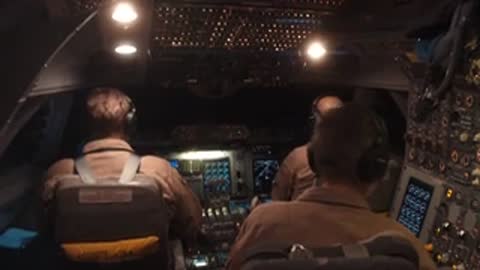 Pilots inside a cockpit wearing headsets while operating controls during flight.