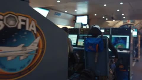 Control room staff monitoring flight equipment and large screens showing space views.