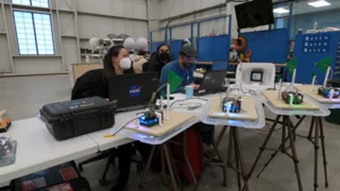 Researchers sitting at a table with laptops and equipment inside a workspace.