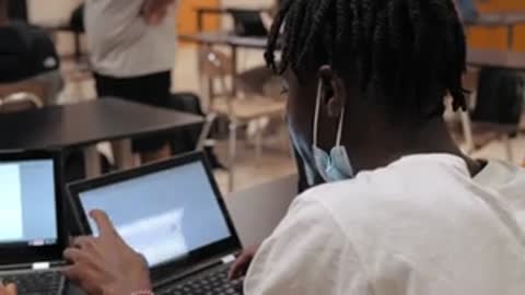 Students working on electronics projects, soldering wires and using laptops.