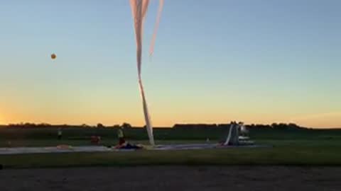 A large weather balloon inflating on a tarmac during sunrise.