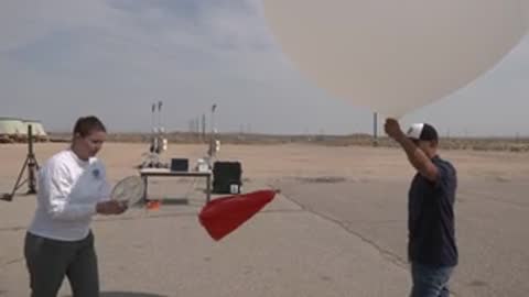 People holding equipment and a red flag on a tarmac next to a balloon.