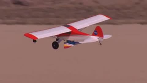 A red and white airplane taking off from a desert runway.