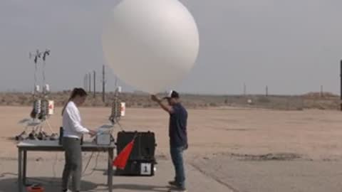 People standing on a tarmac next to a tethered white balloon.