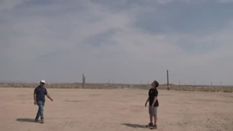 People outdoors on a desert flatland handling equipment and a wing model.