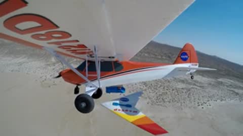 An airplane flying over desert landscape with mountains in the background