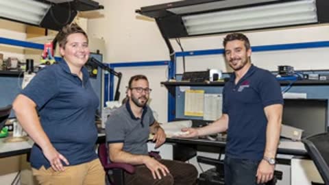 Three people standing together in a workshop or laboratory setting