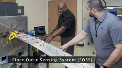 Two people demonstrating a fiber optic sensing system on a long panel
