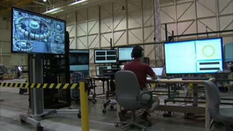 Control room with personnel working at computer stations and large display screens