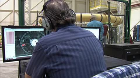 Technician wearing a headset monitoring data on a computer screen in a control room
