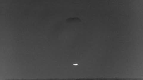 Thermal imaging of a small bright object dropping against a dark sky.