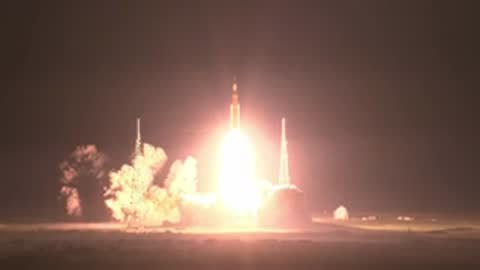 Long-range view of a rocket launching from a pad at night.