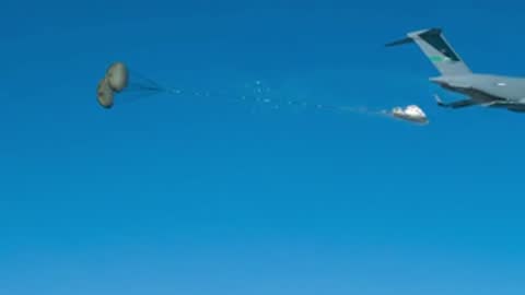 A transport plane releases a small payload in midair over water.