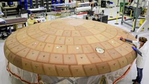 Workers assembling the heat shield tiles of a spacecraft component.