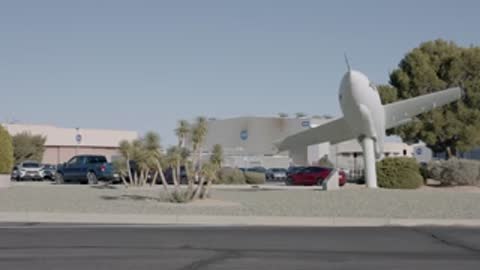 White aircraft model displayed outdoors with buildings and desert landscape