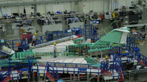 Workers assembling the green structural frame of an aircraft in a factory