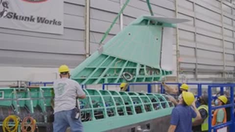 Workers positioning components on the green aircraft frame in the factory