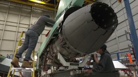 Mechanics working on an aircraft jet engine inside a maintenance facility