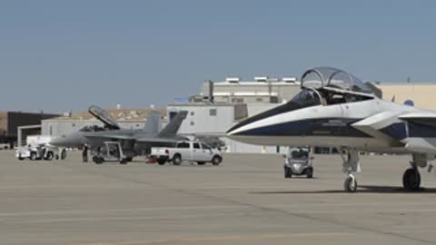White and blue jet aircraft parked on a tarmac at an air base.