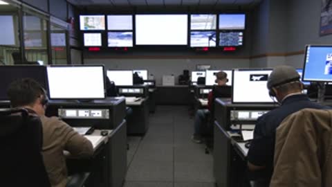 Control room operators sitting at computer stations monitoring flight data screens.