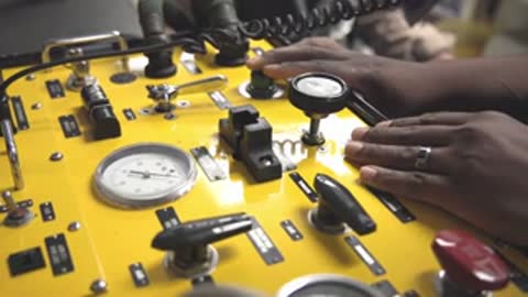 Operator hands operating controls on a yellow instrumentation console.