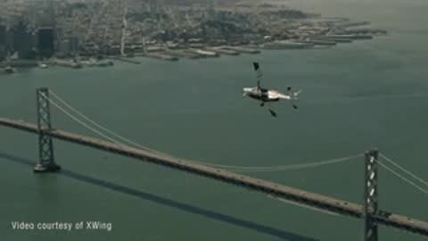 Small aircraft flying in the sky over a bridge and coastal city.