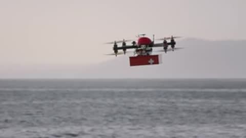 Multi-rotor delivery drone carrying a cargo box while flying over water.