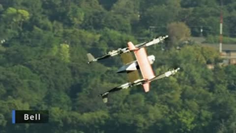 VTOL aircraft with vertical rotors transitioning in flight over a wooded landscape.