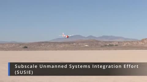 Small subscale aircraft flying above a desert landscape during flight testing.